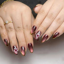 Close-up of hands with maroon nail polish and floral designs on a neutral background, Obroi