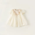 Cream-colored baby dress with tulle details on a white background, Obroi