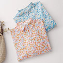 Two floral-patterned shirts on a light gray surface with a woven basket and dried plants, Obroi