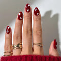Close-up of hands with red nail polish and gold rings on a neutral background, Obroi