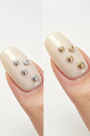 Two side-by-side close-up views of a fingernail displaying four small shell-shaped nail decorations. The left shows silver shells, and the right shows gold shells, Obroi