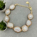 Gold and pearl bracelet on a gray surface with green plants, Obroi
