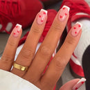 Hand with heart-shaped nail art in front of red shoes, Obroi