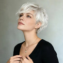 A woman with a short, layered, shaggy platinum blonde wig looking upward. She is wearing a black top and delicate gold jewelry against a plain gray background, with the text '6inch/15, Obroi