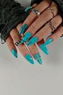 Hand with turquoise acrylic nails featuring decorative elements on a neutral background, Obroi