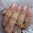 Obroi Nails with decorative elements and a gold ring on a textured background