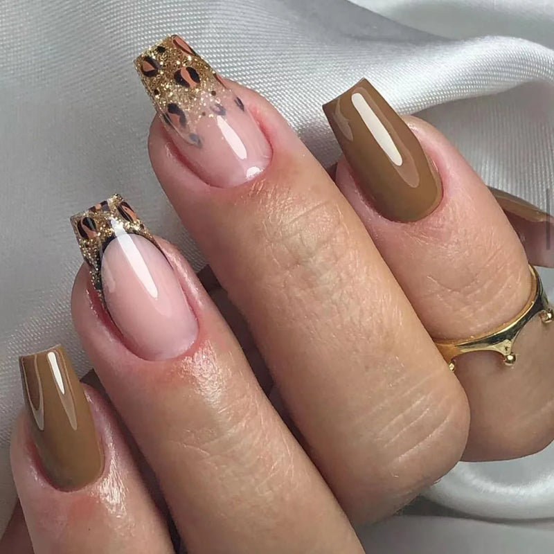 Obroi Close-up of a hand with brown and gold nail art on a neutral background