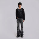 Person wearing a black sheer top and distressed black jeans on a light gray background, Obroi