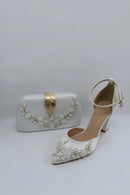 White high-heeled shoes and matching clutch with floral embellishments on a light gray background, Obroi