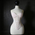 White corset with floral patterns on a mannequin against a dark background, Obroi