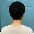 Person with curly black hair wearing a light gray shirt against a blue background, Obroi
