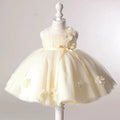 A cream-colored toddler party dress displayed on a white mannequin dress form. The sleeveless dress features a gathered bodice, a matching waist ribbon with a bow, and a voluminous tulle skirt decorated with fabric flowers, Obroi
