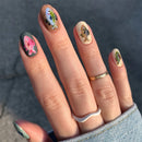 Nails with fish design held against a dark background, Obroi