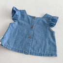 A light blue denim baby top with ruffled sleeves and a button-up front, laid flat on a light textured background, Obroi