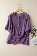 Purple blouse with lace details on a wooden hanger against a beige wall, Obroi