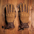 Pair of brown leather gloves with lace-up design on a wooden surface, Obroi