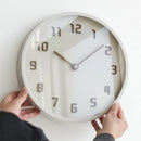 Person holding a round wall clock with white face and wooden frame, Obroi