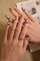 Close-up of a hand with intricately designed nails and gold rings, Obroi