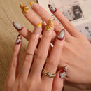 Close-up of a hand with intricately designed nails and gold rings, Obroi
