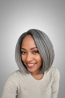 A woman with a short, straight, chin-length bob wig in a cool ash gray color, wearing a light gray knit sweater in front of a dark wood-paneled wall, Obroi