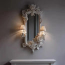 Decorative mirror with floral frame on a wall with two lamps, Obroi