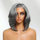 A shoulder-length gray wig with layered, wavy side-swept bangs displayed on a mannequin bust against a light gray background, Obroi