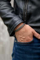 Hand wearing a black braided bracelet with a leather jacket and jeans, Obroi