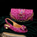 A pink rhinestone-embellished slingback heeled sandal displayed beside a matching pink chain clutch purse on a dark green velvet surface against a black background, Obroi
