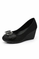 A single women's black wedge pump shoe with a textured woven upper and a decorative black lace bow embellished with rhinestones on the toe. The shoe is shown from a side angle against a plain white background, with the brand name 'Obroi' printed in the upper left.