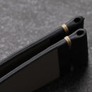 Two black chopsticks with gold bands on a textured gray surface, Obroi