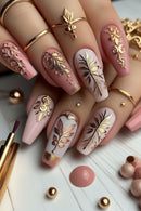 Nails with intricate gold and rose gold designs on a light wooden surface, Obroi