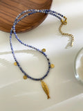 Necklace with blue beads and gold fish pendants on a white surface, Obroi
