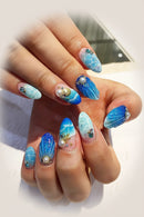 Close-up of a hand with blue and white nail art featuring sea-themed decorations, Obroi