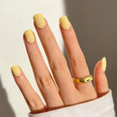 Hand with yellow nail polish and a gold ring on a neutral background, Obroi
