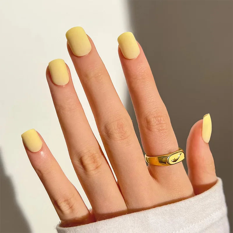 Hand with yellow nail polish and a gold ring on a neutral background, Obroi