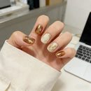 Hand with gold and white nail design in front of a laptop, Obroi