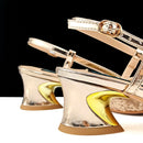 Close-up of metallic gold high-heeled sandals with sculptural curved wedge heels and buckle straps, photographed against a black background with a white surface at the bottom, Obroi