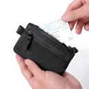 Black zippered pouch held by a hand with a driver's license peeking out on a white background, Obroi