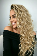 Woman with long, wavy blonde hair smiling in a room with clothing racks, Obroi