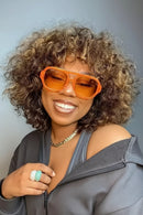 Woman wearing orange sunglasses and a gray top against a light blue background, Obroi