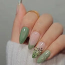 Hand with green and gold nail art on a neutral background, Obroi