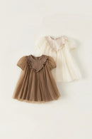 Two children's dresses, one brown and one white, on a light beige background, Obroi