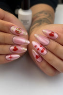 Pink nail art with red hearts and gold accents on a neutral background, Obroi
