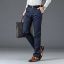 Man wearing navy pants and brown shoes holding a black briefcase against a gray background, Obroi