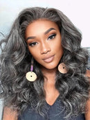 A close-up portrait of a woman with long, wavy, medium-to-coily black hair styled with a natural-looking lace front. She is wearing large, round, light beige wooden earrings with purple hanging accents, Obroi