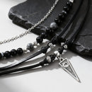 Black beaded necklaces with leather straps and silver pendants on a dark stone surface, Obroi