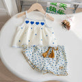 Children's outfit with white top and floral shorts on a white surface, Obroi