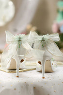 White high-heeled shoes with decorative ribbons on a soft surface, featuring the brand 'Obroi'.