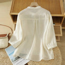 White blouse on a hanger with a wooden shelf and magazine in the background, Obroi