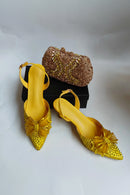 Yellow high-heeled shoes with decorative elements and a matching clutch on a white background, Obroi